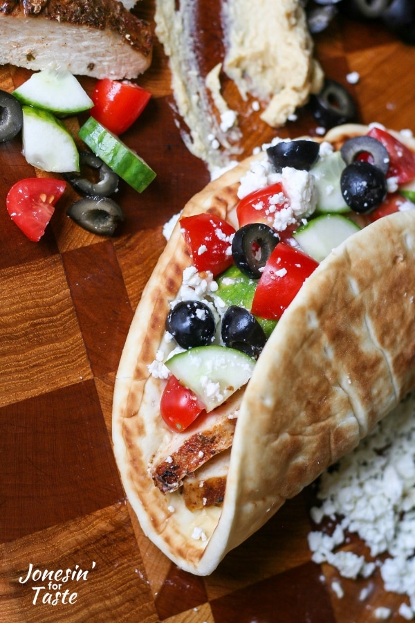 A pita with chicken and toppings on a cutting board