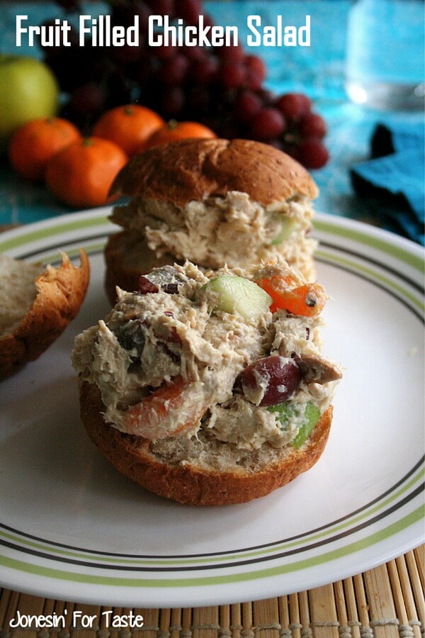 chicken salad sandwiches on a plate on a blue tablecloth with fruit in the background