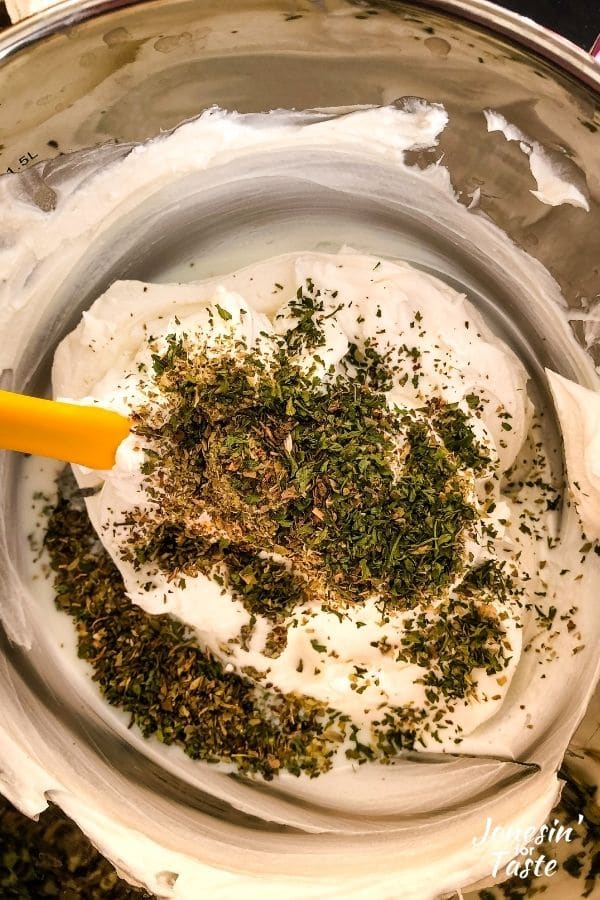 a metal bowl with goat cheese and lots of dried herbs ready to be mixed together
