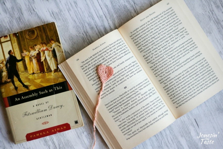 An open book with a crochet heart bookmark next to an additional closed book.