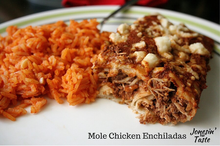 Two mole enchiladas cut in half on a plate next to Mexican rice