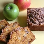 Slices of pumpkin apple bread next to a loaf and apples