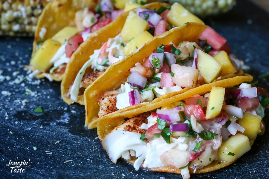 Four fish tacos topped with coleslaw and peach salsa