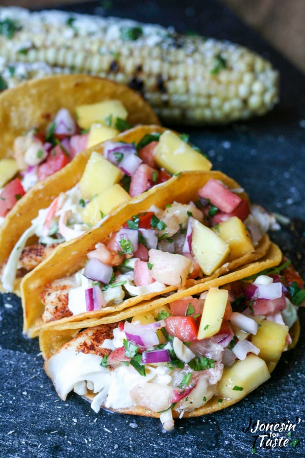 Fish tacos and grilled corn on a black cutting board