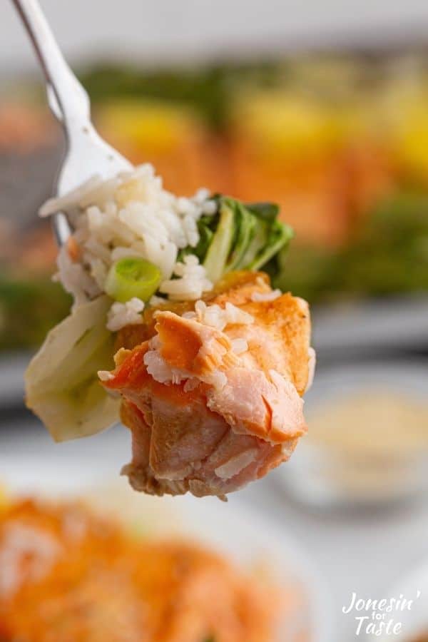 a fork with a bite of salmon, bok choy and rice