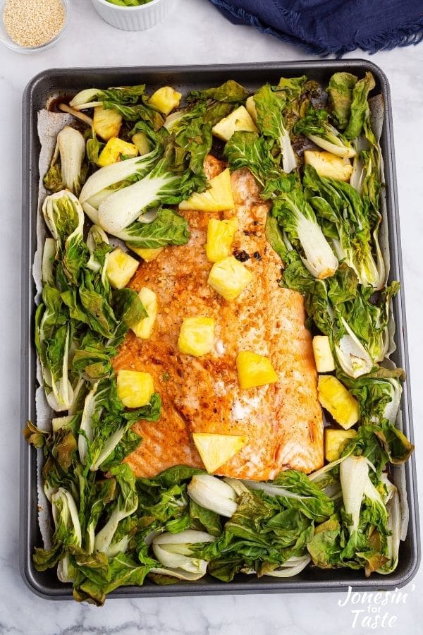 A cookie sheet with salmon, pineapple, and baby bok choy