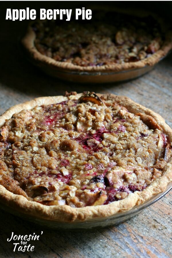 Two apple berry pies topped with oatmeal crumble and with purple and blue berries peaking out of the oatmeal crumble.