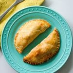 a blue plate with two baked empanadas next to a yellow napkin