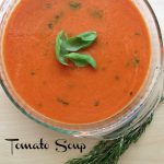 a glass bowl of tomato soup with 3 Basil leaves in the center