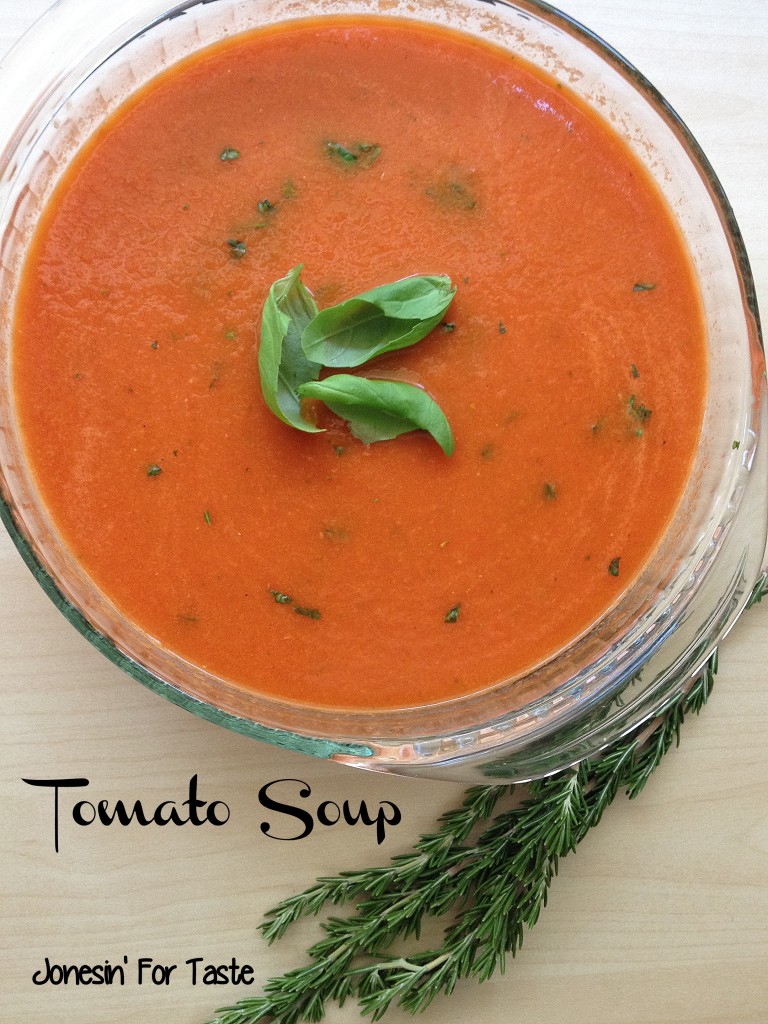 a glass bowl with tomato soup and 3 basil leaves arranged in the center