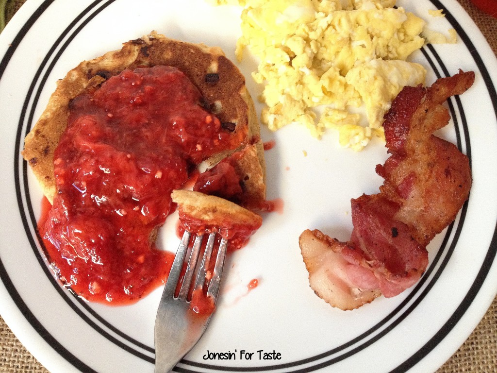 pancakes topped with strawberry sauce with scrambled eggs and bacon