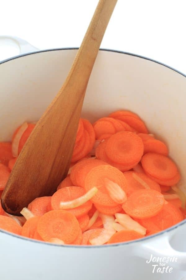 a white pot with carrots and onion sautéing