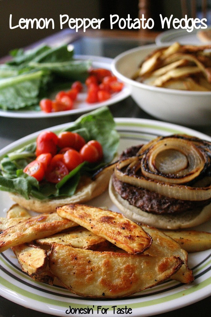 A plate with slices of Lemon Pepper Potato Wedges with a hamburger and a bowl of potato wedges in the background along with a plate of hamburger toppings.
