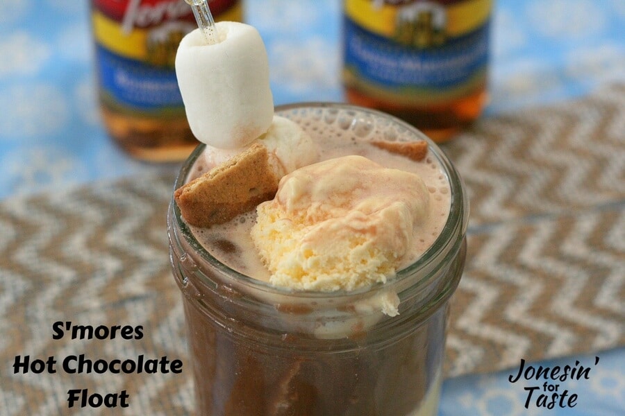 A S'mores Hot Chocolate Float on a blue snowflake tablecloth with 2 Torani syrups in the background
