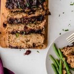 cranberry turkey meatloaf laid out on a wooden cutting board. Slices are falling over and everything is sprinkled with fresh herbs.