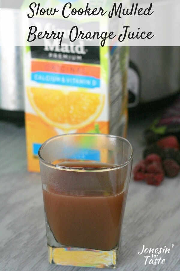 Simple Slow Cooker Mulled Berry Orange Juice in a glass cup in front of a container of orange juice