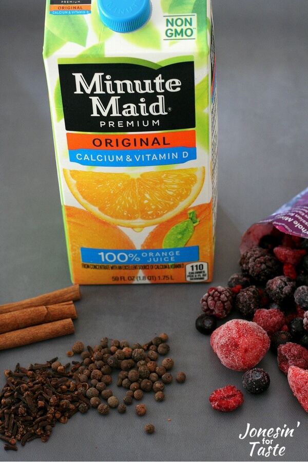 Showing the ingredients for Slow Cooker Mulled Berry Orange Juice including frozen berries, spices, and orange juice.