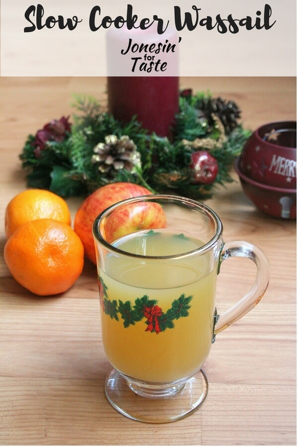 Easy Slow Cooker Wassail in a glass mug with oranges and apples and Christmas decor in the background
