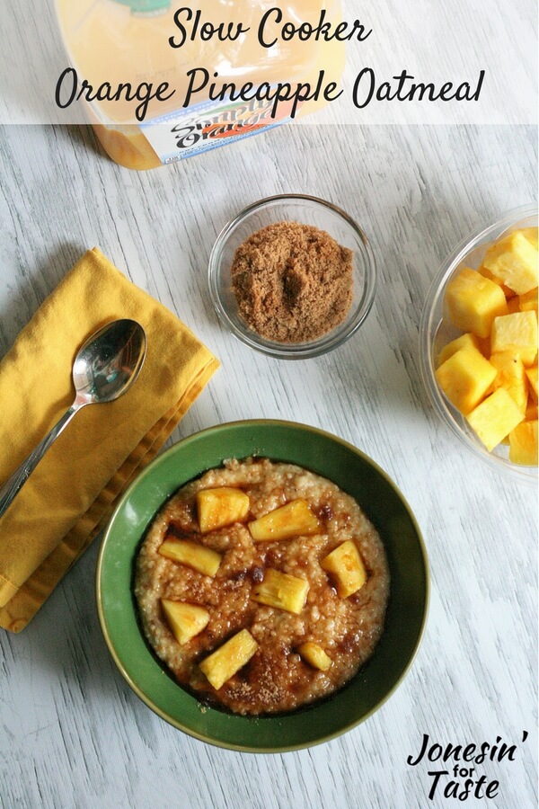 A green bowl of Slow Cooker Orange Pineapple Oatmeal on a white table with sides of fresh pineapple and a small bowl of brown sugar.