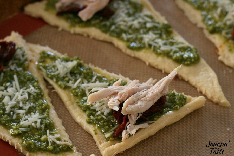A croissant triangle with pesto spread topped with parmesan cheese sun dried tomatoes and shredded chicken.