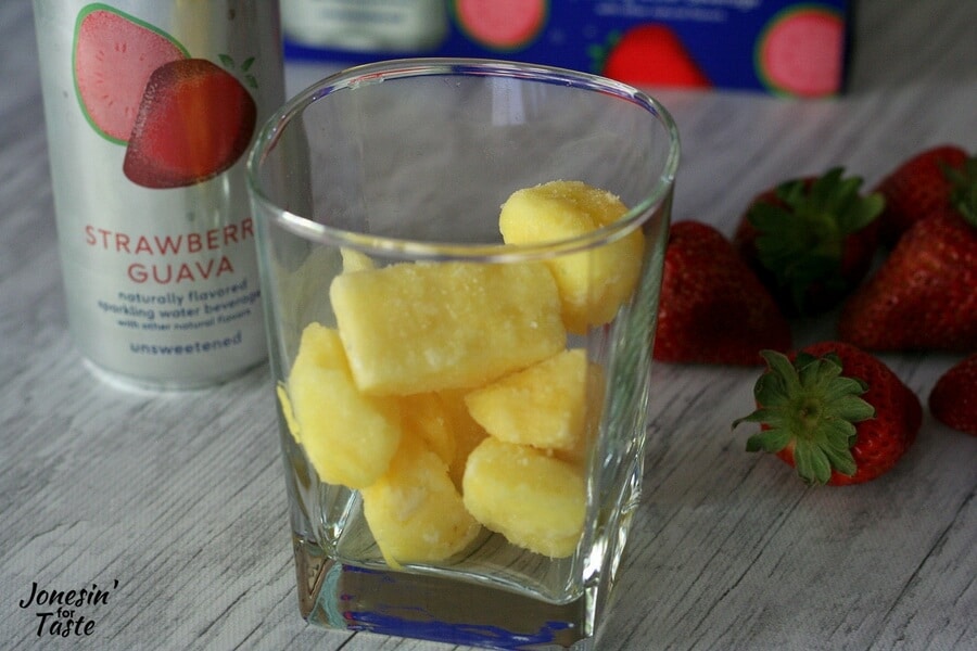 A glass of frozen pineapple with strawberries in the background