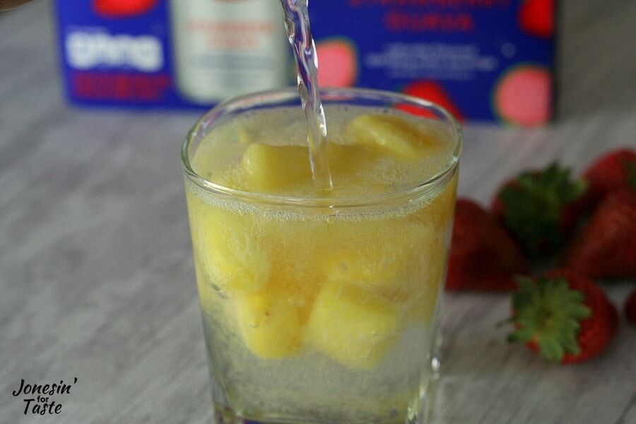 A closeup view of DASANI Sparkling being poured into a glass with frozen pineapple