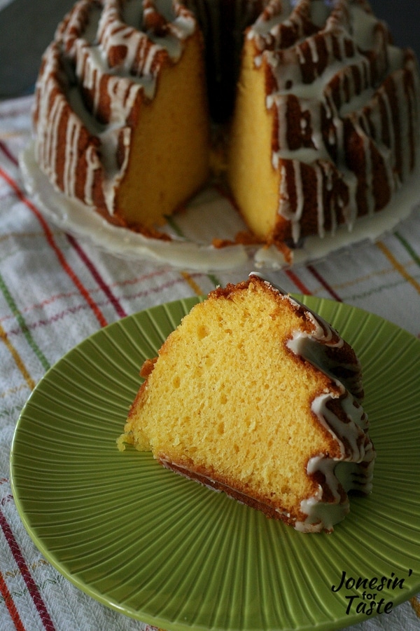 A slice of orange pound cake on a plate in front of the cake