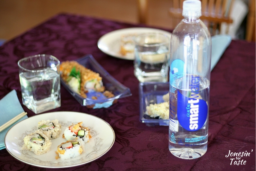 plates of sushi on a table with a bottle of smartwater in the forefront