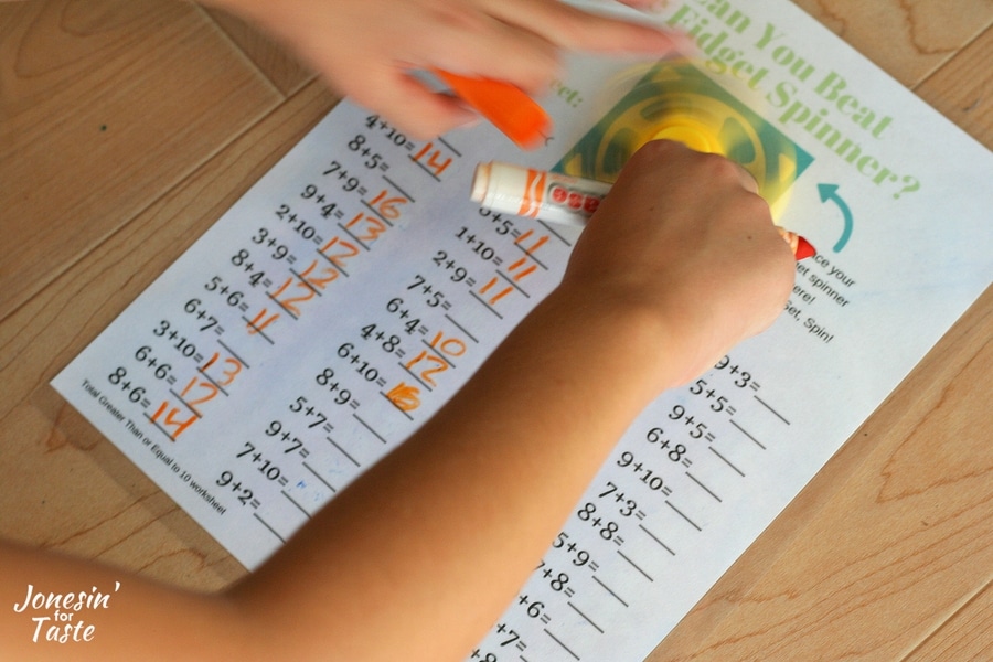 A child spinning a fidget spinner while working on an addition worksheet