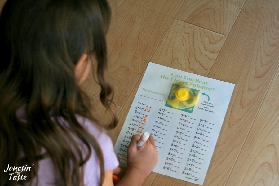 A girl writing down answers on a fidget spinner addition worksheet