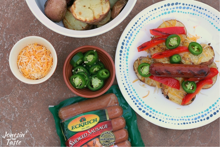 A plate of grilled smoked sausage and potatoes topped with grilled red peppers, cheese, and jalapeno with the ingredients surrounding the plate