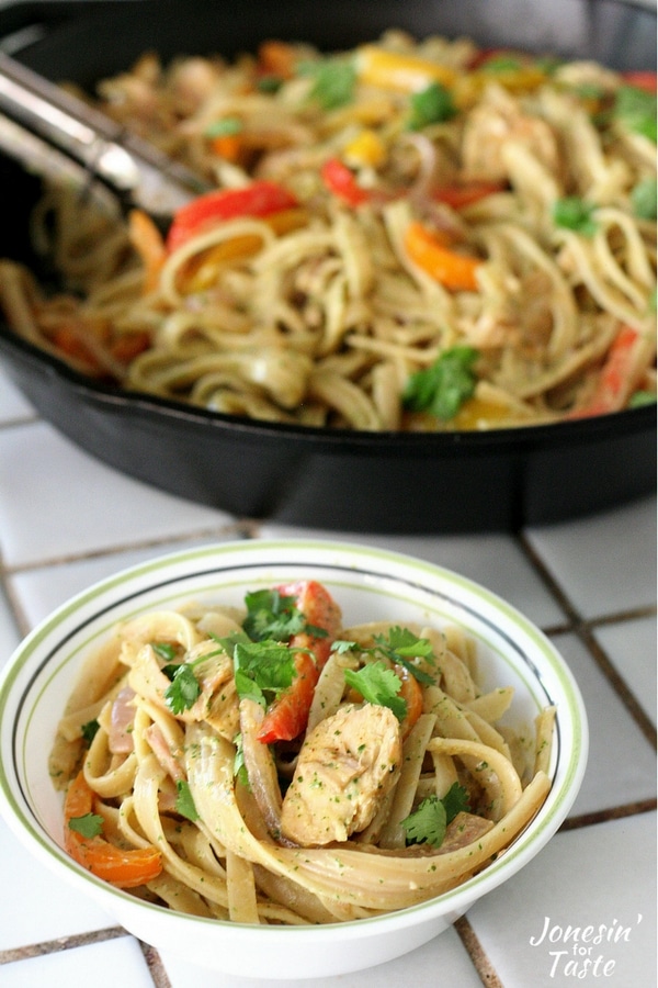 A bowl of chicken fajita pasta with cilantro lime sauce in front of a large cast iron pan full of chicken fajita pasta.