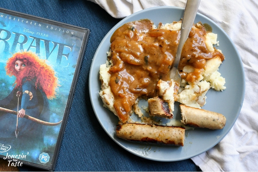 A bite of bangers and mash on a plate next to a DVD of Brave and a white napkin