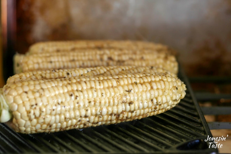 Cobs of corn on a grill brushed with cumin butter flavored coconut oil