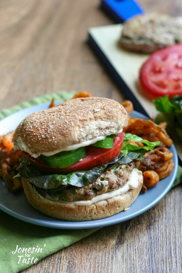 A spicy jalapeno black pepper turkey burger topped with tomato, lettuce, sliced jalapenos, and a spicy mayo spread on a blue plate with sweet potato fries.