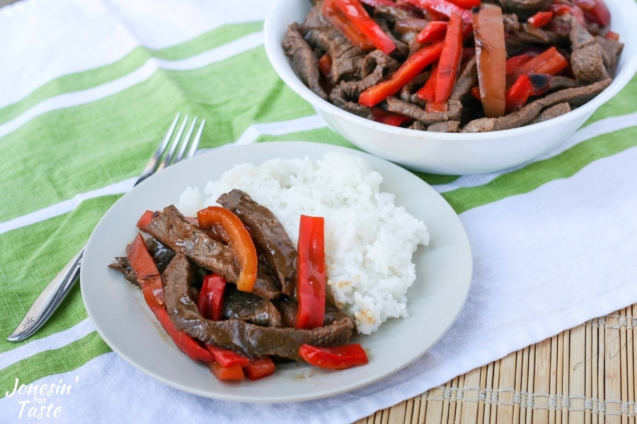 A plate of Asian pepper steak next to a fork on a bamboo placemat