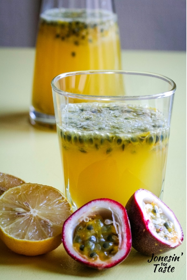 a glass of lemonade with halved lemons and passion fruit in front of it