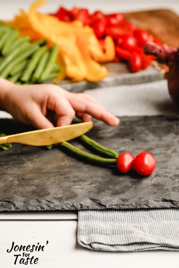 a child cutting green beans with a knife on a black cutting board