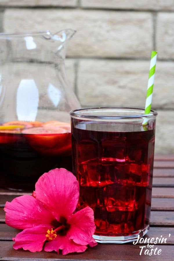 a glass of juice next to a pitcher and a hibiscus flower