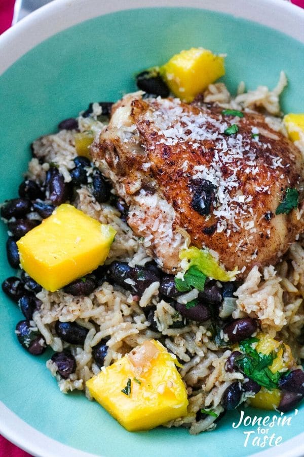 a bowl of coconut rice, black beans, and chicken topped with diced mangoes