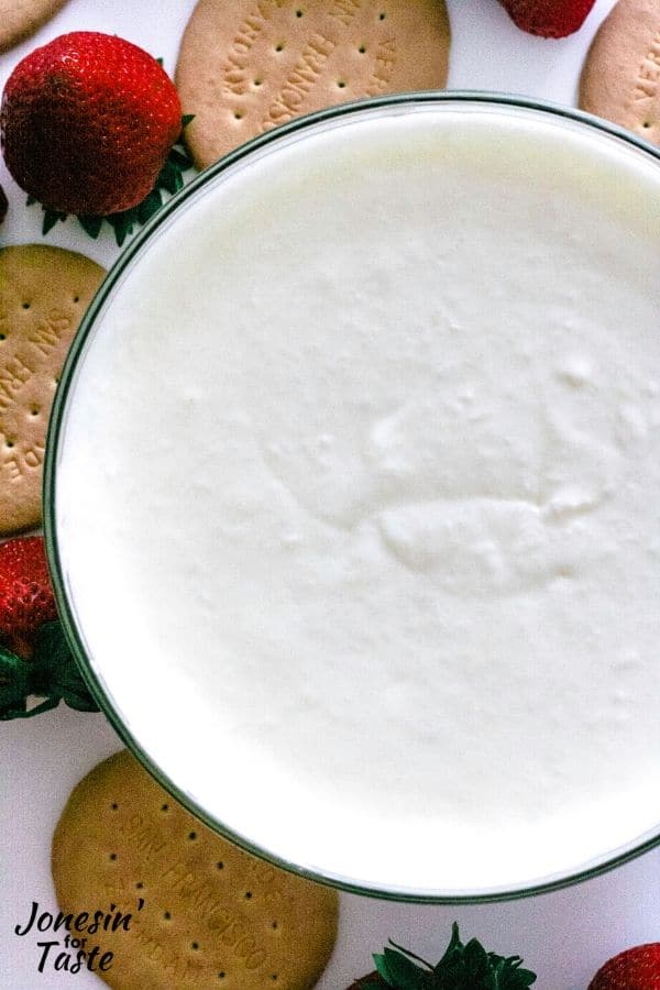 a bowl of coconut fruit dip surrounded by strawberries and crackers
