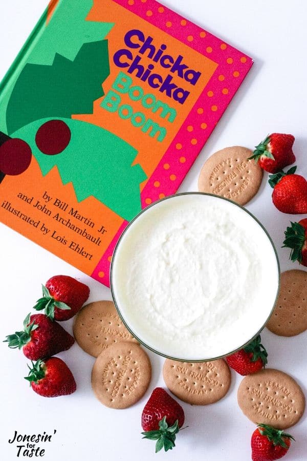 a bowl of coconut dip next to a book, strawberries, and crackers
