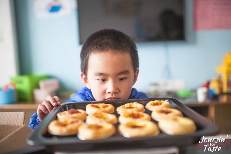 a child looking at a pan filled with pastries