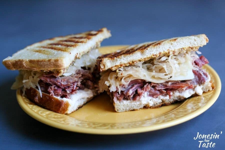 a corned beef and sauerkraut sandwich halved and sitting on a yellow plate