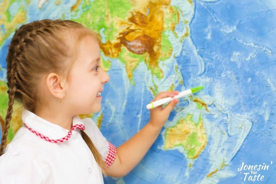 a little girl using a pen to point to a place on a world map