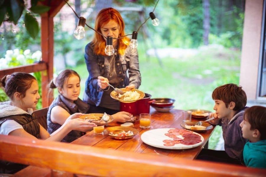 a mother serving her children food as they eat food on a porch