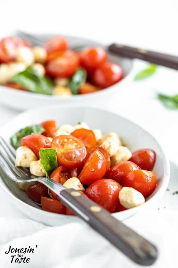 two white bowls filled with caprese salad and a fork resting on top