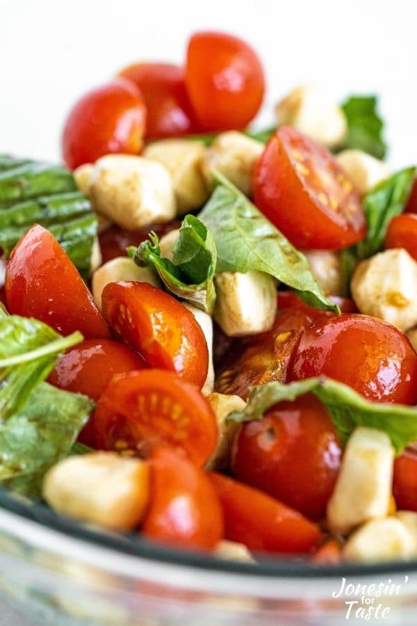 a close up shot of mozzarella, tomatoes, and basil coated in a balsamic vinaigrette