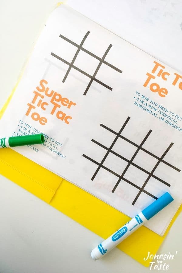 a yellow folder with a tic tac toe printable inside a sheet protector with 2 dry erase markers sitting on the page
