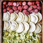 a cookie sheet with 3 rows, pink sausage slices at the top, half moon pierogis in the center, and sliced cabbage at the bottom